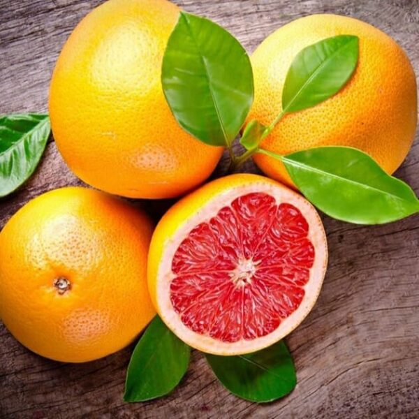 Citrus 'Star Ruby' Grapefruit 4L Pot grapefruits with green leaves lie on a wooden surface, one sliced to show its bright red center.