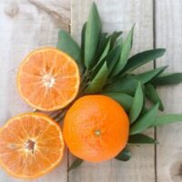One whole and two halved Citrus Mandarin 'Murcott' oranges with fresh leaves on a wooden surface.