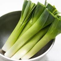 A bowl containing fresh leeks with vibrant green tops and white stems, displayed in a Leek 3" Pot set against a white background.