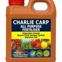 A bottle of Charlie Carp All Purpose Liquid Fertilizer Concentrate 1L. The label highlights benefits such as stimulating growth, boosting plant immune systems, and improving soil. This all-purpose concentrate comes with a red cap and a handle for easy use.