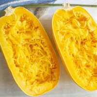 The contents of a clear glass baking dish, featuring two halves of squash spaghetti with shredded flesh inside, bring to mind the lush greens found in a Squash 'Spaghetti' 4" Pot.