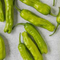 Several Capsicum 'Shishito' chilli peppers are scattered on a light gray surface.