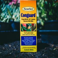 A box of Searles Conguard Garden & Lawn Insecticide 500ml, in front of a plant.