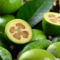 Fresh feijoas (pineapple guavas) with one cut in half, revealing the flesh and seeds, on a wooden surface. feijoa acca