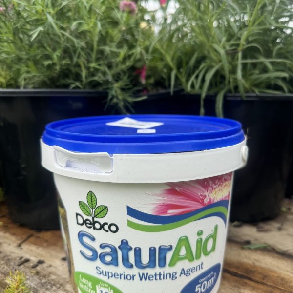A bucket of debco saturaid wetting agent placed in front of blooming pink flowers, suggestive of use in gardening.