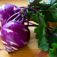 Two vibrant purple kohlrabi bulbs with green leaves attached, artfully arranged on a wooden surface, showcase the beauty of Kohlrabi 4" Pot (Copy).
