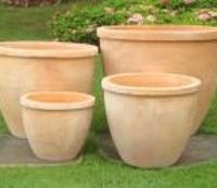 The Terracotta Rim Egg Traditional 23x19cm plant pots, arranged in varying sizes with a ribbed design, are displayed on a grassy lawn with greenery in the background.
