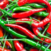 A close-up of a pile of red and green chili peppers with stems, arranged in a scattered pattern.