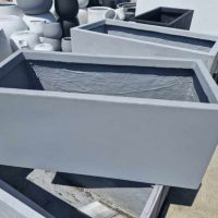 The sunlit outdoor surface features multiple rectangular gray concrete planters, such as the GardenLite Trough Cement M model with dimensions of 80x37x37cm.