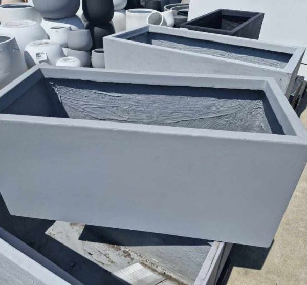 The sunlit outdoor surface features multiple rectangular gray concrete planters, such as the GardenLite Trough Cement M model with dimensions of 80x37x37cm.