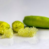Close-up of finger limes with one cut open, revealing pearl-like citrus vesicles on a smooth white surface.