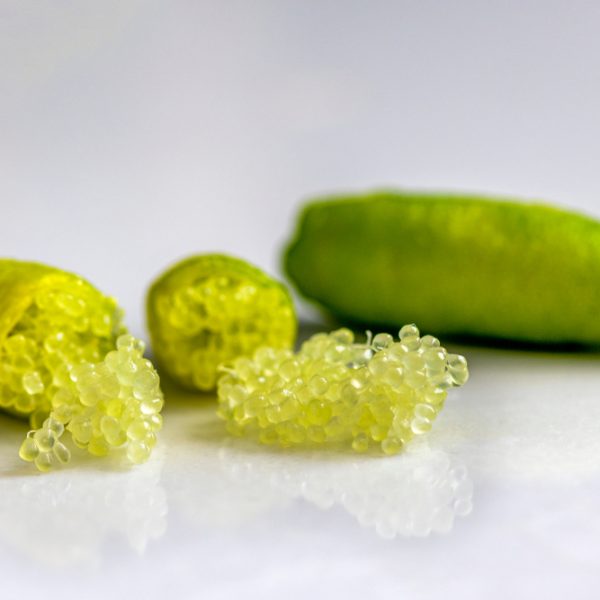 Close-up of finger limes with one cut open, revealing pearl-like citrus vesicles on a smooth white surface.