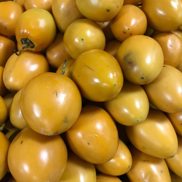A vibrant pile of ripe Solanum 'Tamarillo' Red (Copy) catches the eye, stacked closely together with a hint of orange-yellow peeking through.