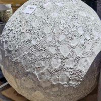 Close-up of a large, textured stone sphere with a rough, crater-like surface resembling the Sorrento 'Sadiki Urn Antique' M 40x36cm. A small price tag adorns this intriguing outdoor display piece.