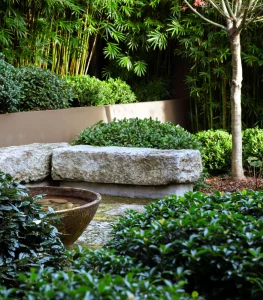 A landscaped garden with green bushes, a tree, stone benches, and a decorative bowl reflects the beauty of Japanese gardens, set against a background of tall bamboo.