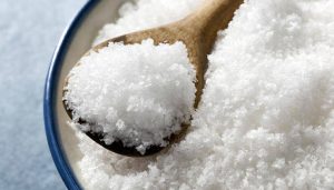 A close-up of coarse white salt in a bowl, with a wooden spoon resting on top and filled with salt—perfect for trying out simple Garden Hacks.