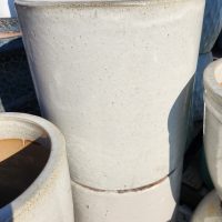 Two large, stacked, off-white ceramic pots with a smooth, slightly speckled surface, shown outdoors in sunlight.
