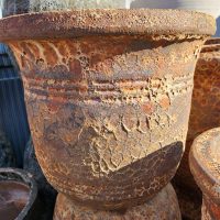 A close-up of a large, weathered terracotta planter with a rough, textured surface and decorative horizontal ridges.