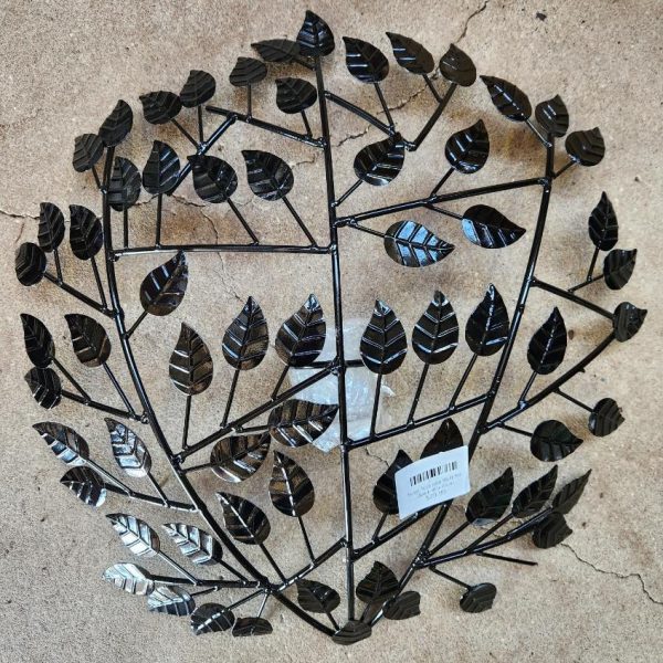 The Raja TeaLight Wall Art Black 46x10cm is a round metal wall decor with a symmetrical tree branch pattern and black leaves, displayed on a concrete surface. A white barcode sticker is near the bottom center.