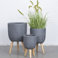 Three GardenLite Egg Planter with Legs Brushed Concrete (SET OF 3) are arranged together; one holds tall green grass, and two are empty.