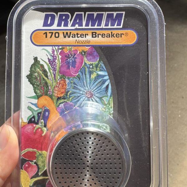 A hand holds a packaged DRAMM 170 Water Breaker Nozzle, featuring a metal spray head and colourful floral artwork on the label.