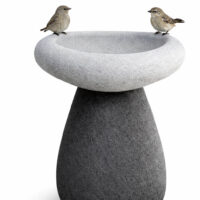 Two small birds perched on the rim of a modern, two-tone stone bird bath against a white background.