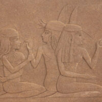 Stone relief depicting three seated ancient Egyptian women, each wearing traditional headdresses and garments, with one woman gesturing and the others engaged in conversation.