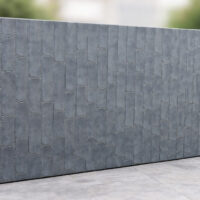 A large rectangular grey concrete wall with a textured, repeating bamboo-like pattern stands outdoors on a paved surface, with blurred greenery in the background.